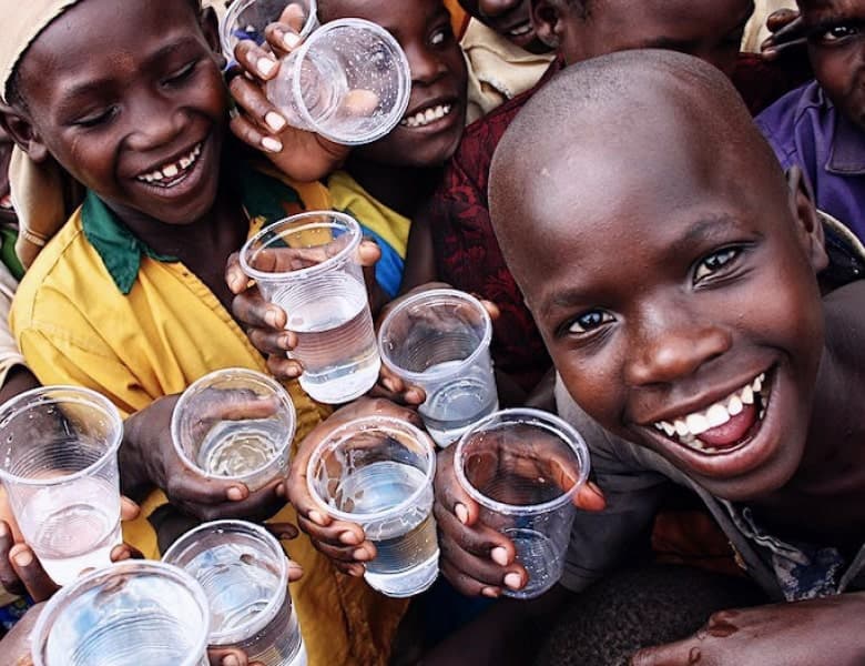 Children holding glasses of clean water during a WASH outreach session, smiling at the camera.